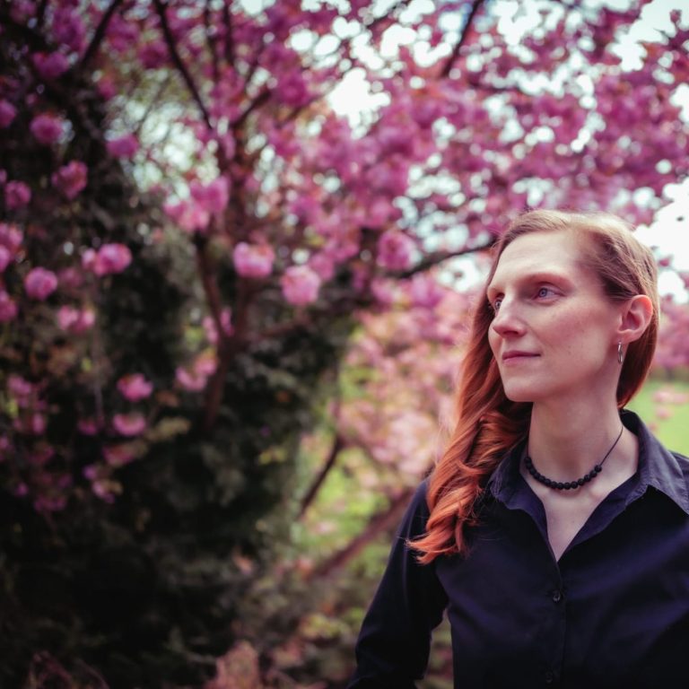 Blick in die Natur Frau mit roten Haaren sitzt am Ufer eines ruhigen Sees umgeben von Bäumen.